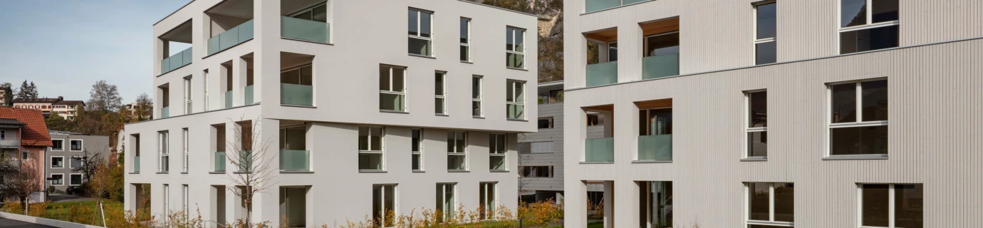 Zwei moderne weiße Wohngebäude mit Balkonen, umgeben von grünen Rasenflächen an der Zürcherstrasse in Bludenz (Wohnanlage).