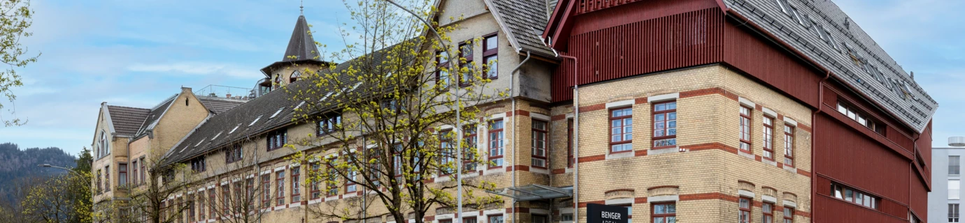 Das JUFA Hotel Bregenz mit gelber Backsteinfassade und einem roten Anbau an einer Straße (SIBLIK)