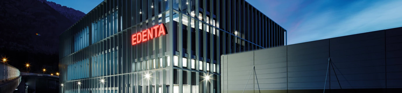 Modernes Geschäftsgebäude von Edenta bei Dämmerung mit beleuchtetem Logo und klarer Architektur unter blauem Himmel.
