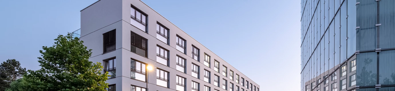 Modernes, weißes Verwaltungsgebäude mit reflektierenden Fenstern und daneben ein verglastes Bürogebäude in Dornbirn.