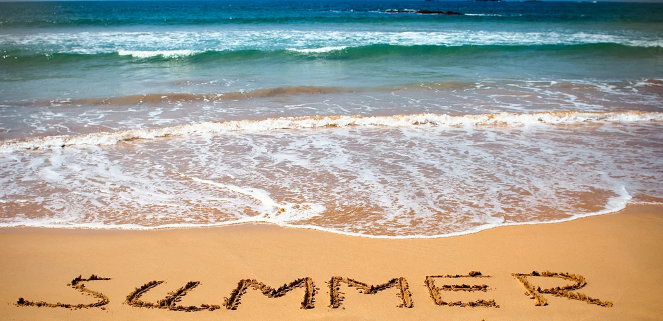 Das Wort "SUMMER" ist in den Sand am Strand geschrieben, mit Meereswellen im Hintergrund.