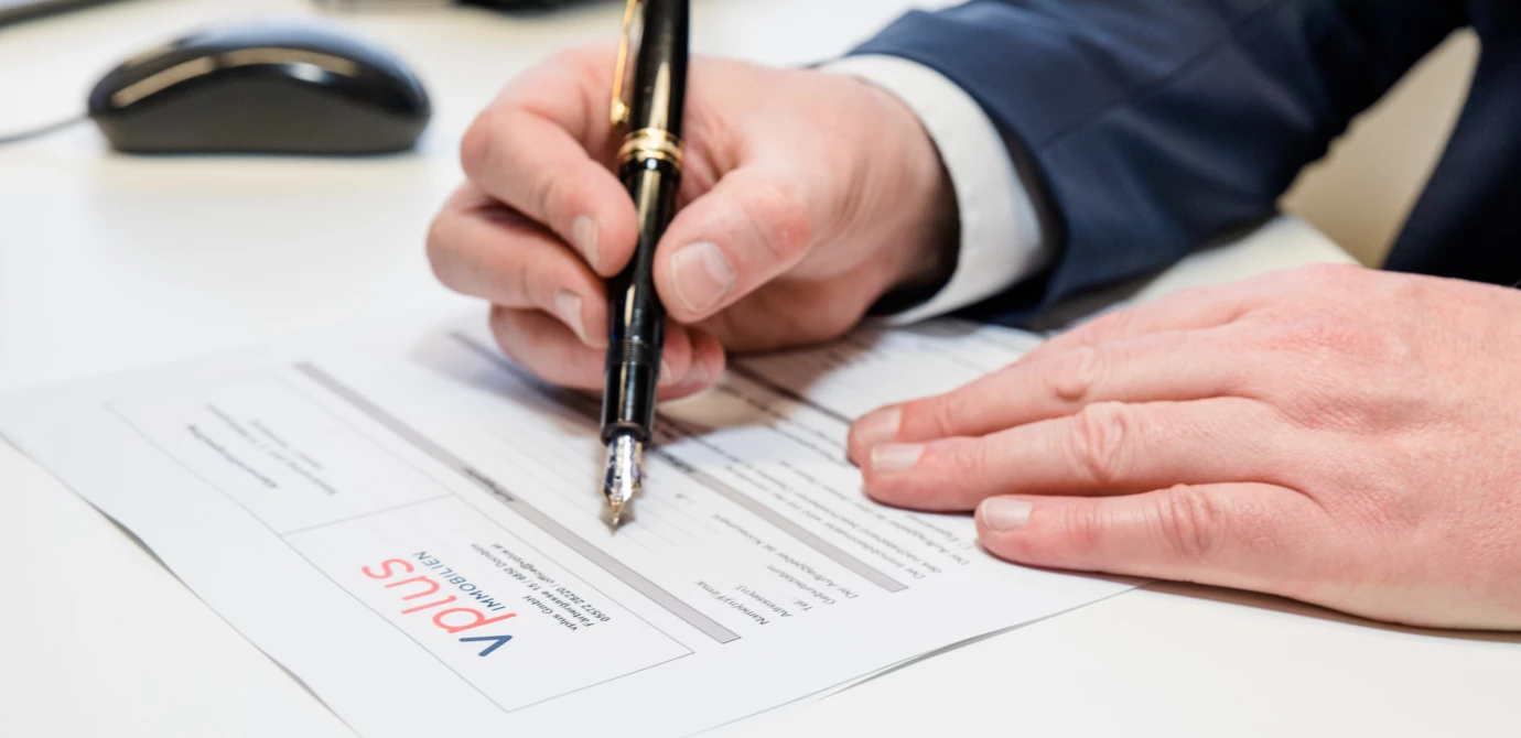 Eine Hand im Anzug, die mit einem Füllfederhalter auf einem Dokument mit dem Vplus Immobilien Logo unterschreibt (Hausverwaltung)