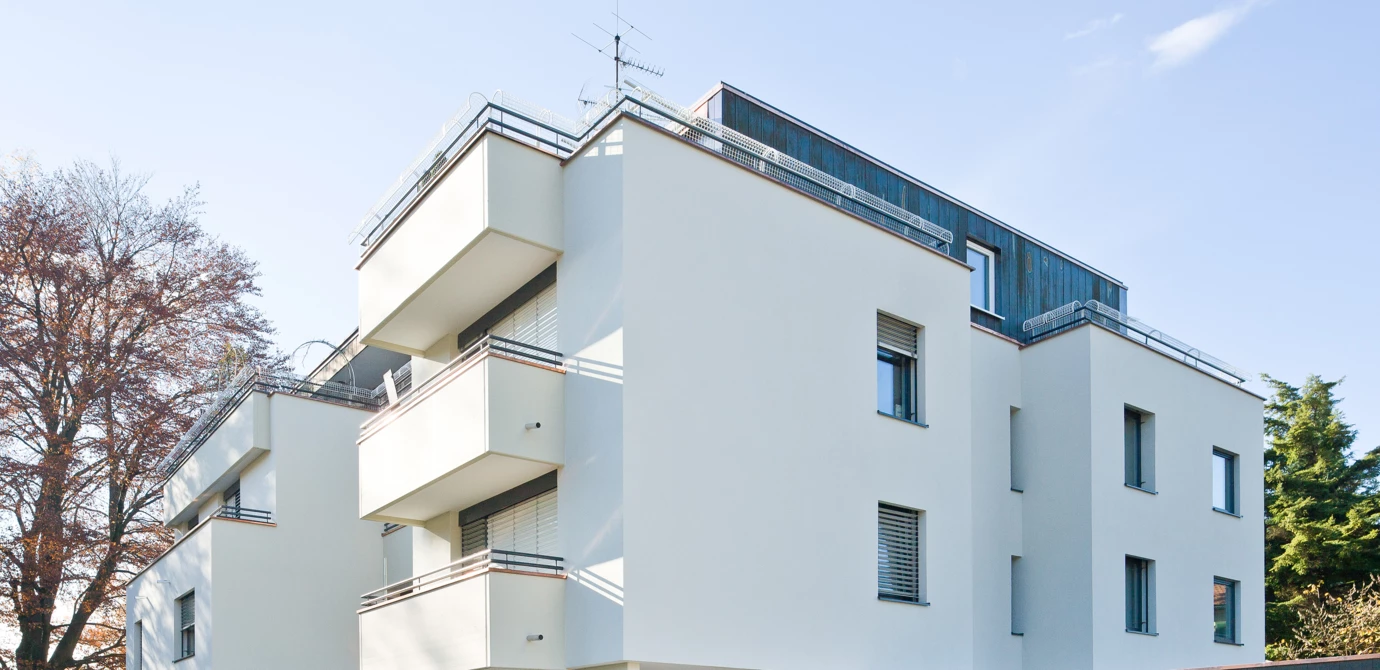 Modernes, frisch saniertes Mehrfamilienhaus mit heller Fassade, Balkonen und integriertem Carport an einem sonnigen Tag (Sanierung, Wärmedämmverbundfassade).