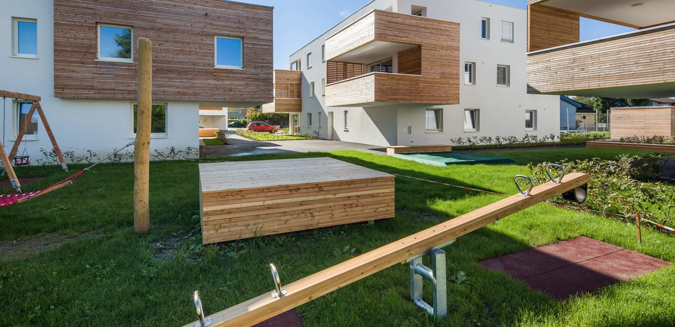 Wohnanlage Eicheleweg in Hard mit modernem Spielplatz und Holzelementen auf grünem Rasen.
