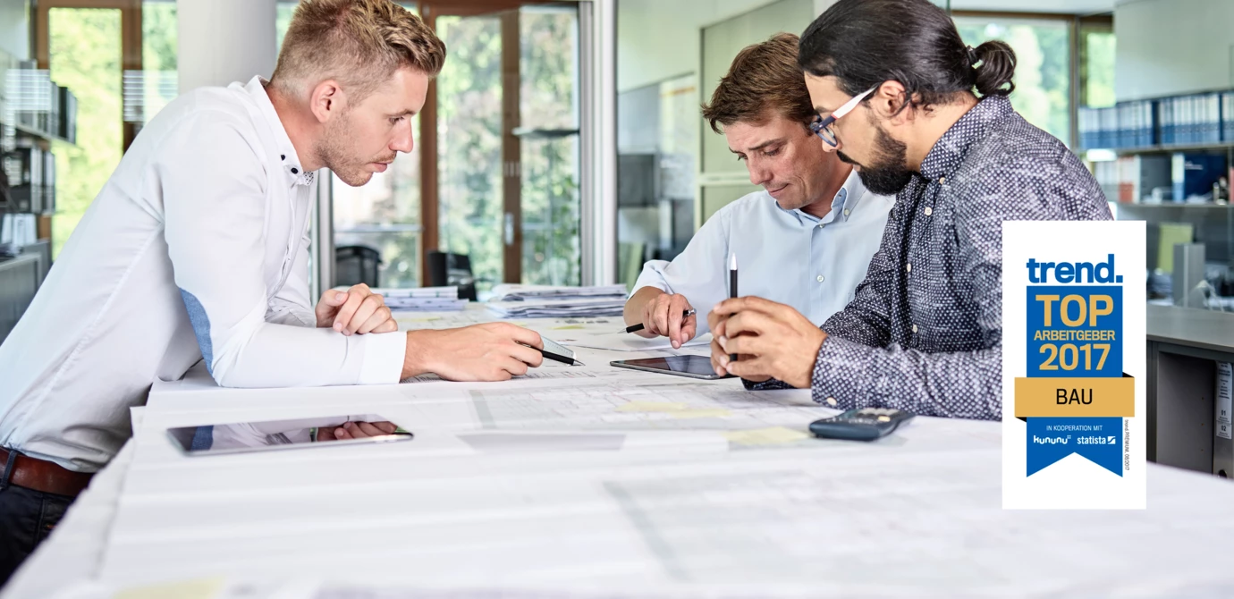 Drei Bauingenieure besprechen Baupläne und arbeiten mit einem Tablet. In der oberen rechten Ecke ist das Logo „trend. TOP ARBEITGEBER 2017 BAU“ zu sehen (Bester).