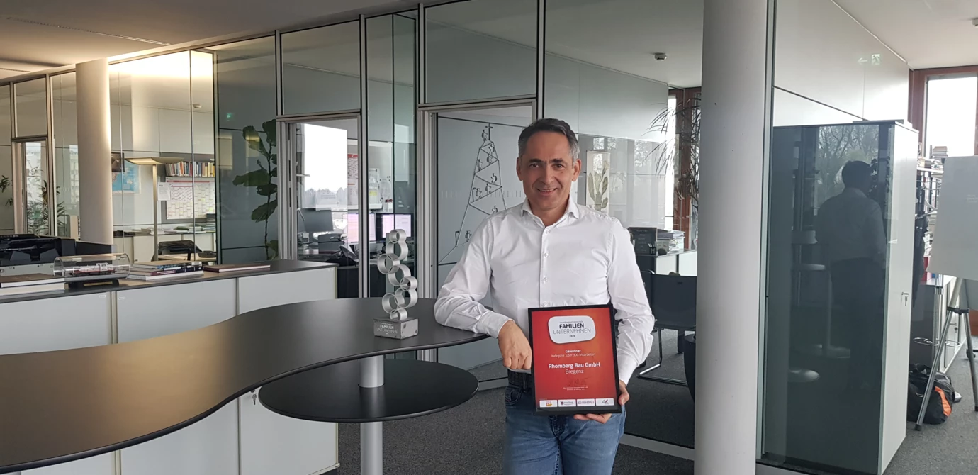 Ein Mann im Büro präsentiert stolz eine Auszeichnung als familienfreundliches Unternehmen für Rhomberg Bau GmbH (Vorarlberg, Familienunternehmen)