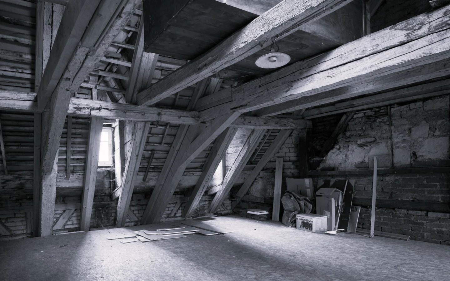 Schwarz-Weiß-Bild eines unfertigen Dachbodens mit Holzbalken, einer Fensteröffnung und Baumaterialien auf dem Boden (Rathausstr)