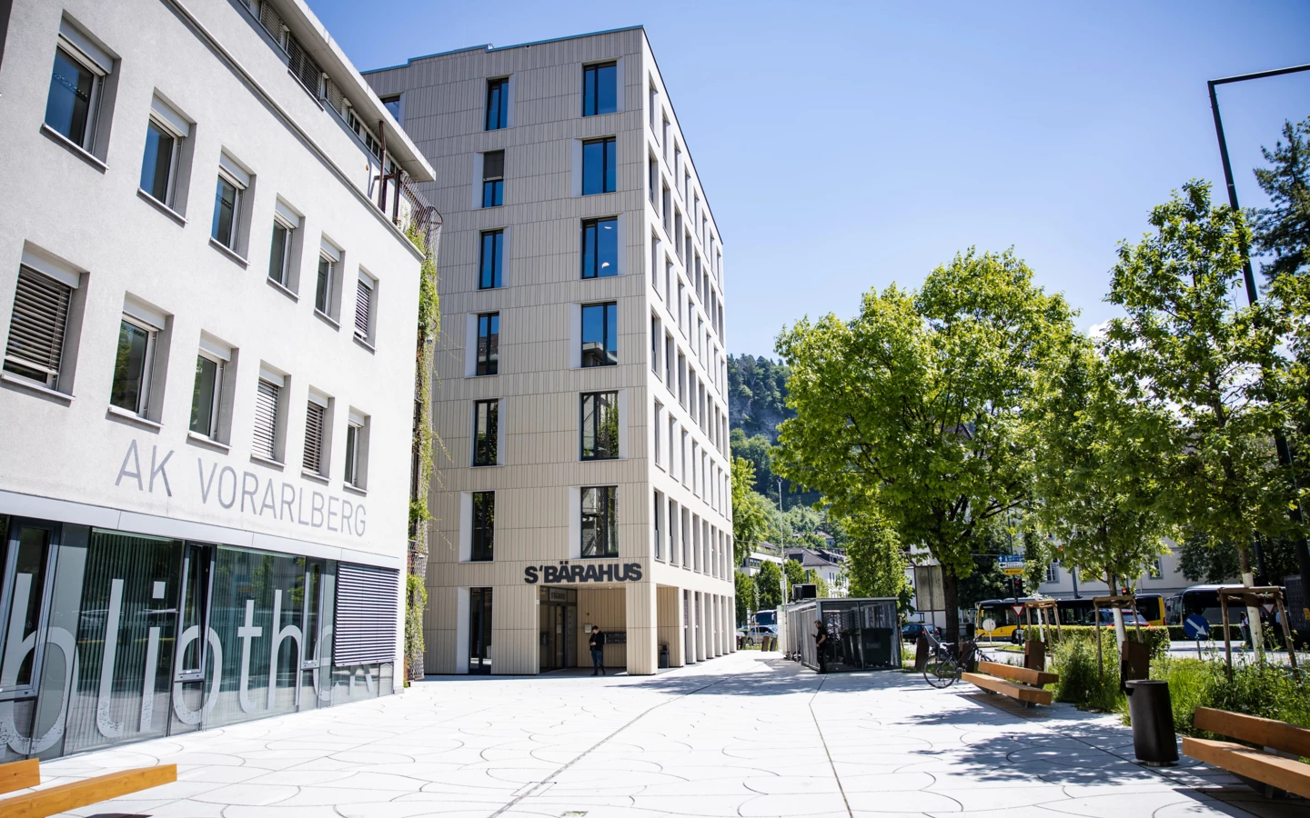 The Baerahus building and AK Vorarlberg building on a sunny day in Feldkirch, with trees, benches, and a street visible.