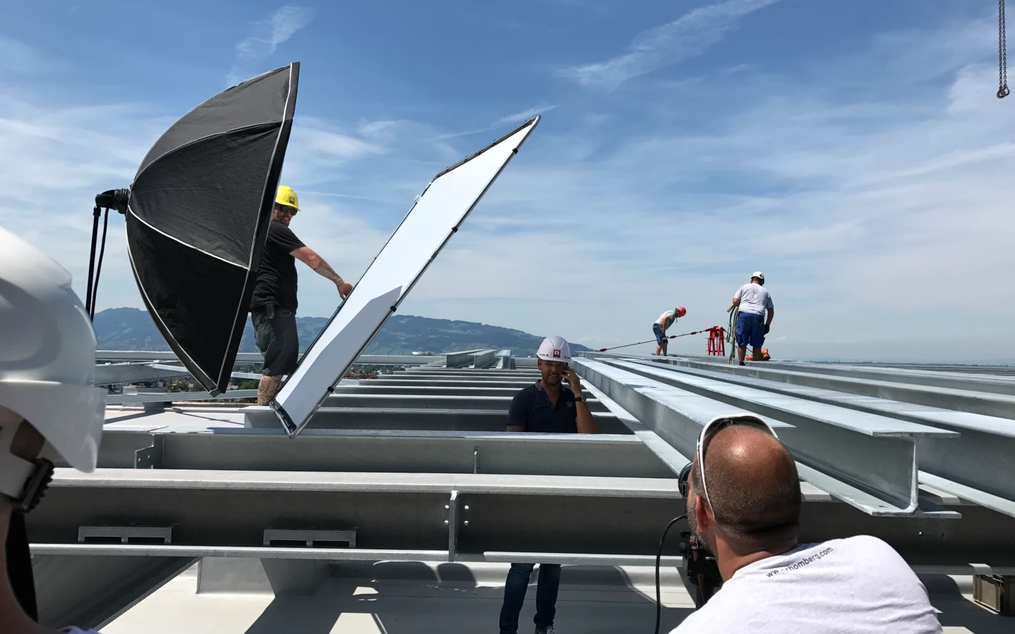 Ein Fotoshooting auf dem Dach eines Gebäudes von Rhomberg Bau GmbH, mit Mitarbeitern und Ausrüstung wie Reflektoren und Blitzschirmen.