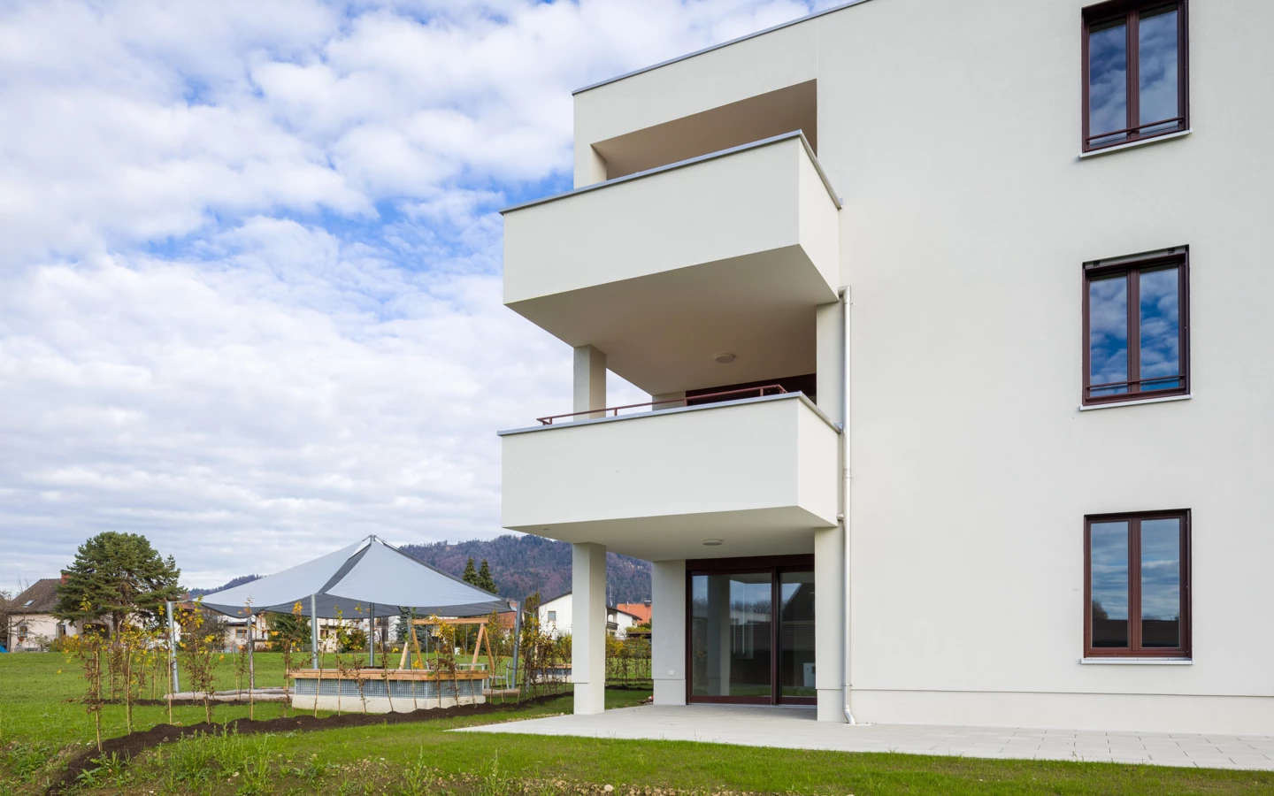 Moderne, weiße Wohnanlage an der Unterhochstegstraße mit Balkonen, Fenstern und Kinderspielplatz unter einem Zelt im Garten.