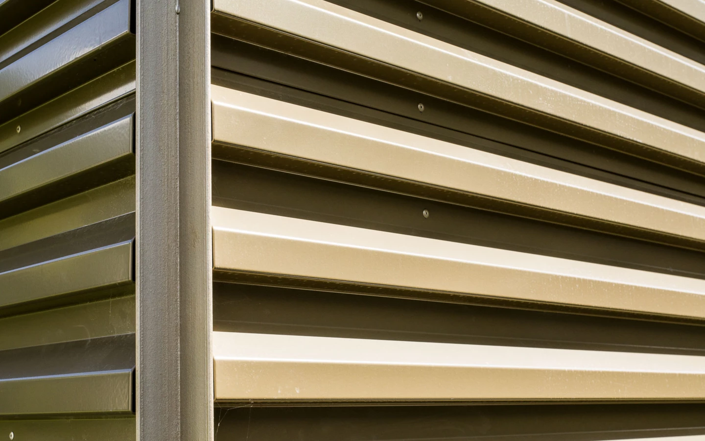 Detailaufnahme einer beigen Metallfassade mit horizontalen Lamellen und vertikalem Profil (Bahnhofstraße, Wohnanlage, Bahnhofsstrasse, Vandans).