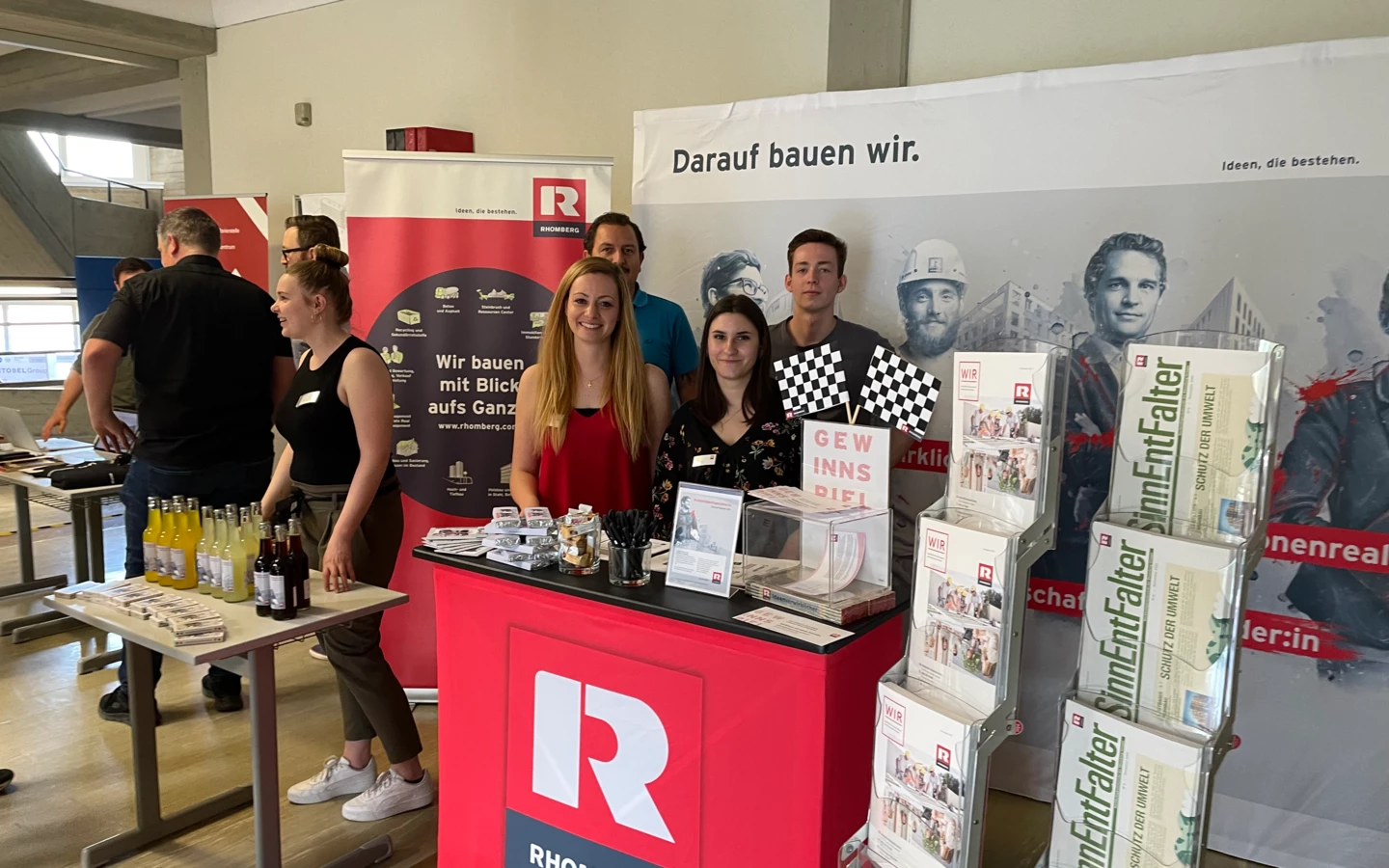 Messestand des Bauforums mit Rhomberg Bau Beschriftung, Informationsmaterialien und Mitarbeitern, die bereitstehen, die Besucher des Messestands zu begrüßen.