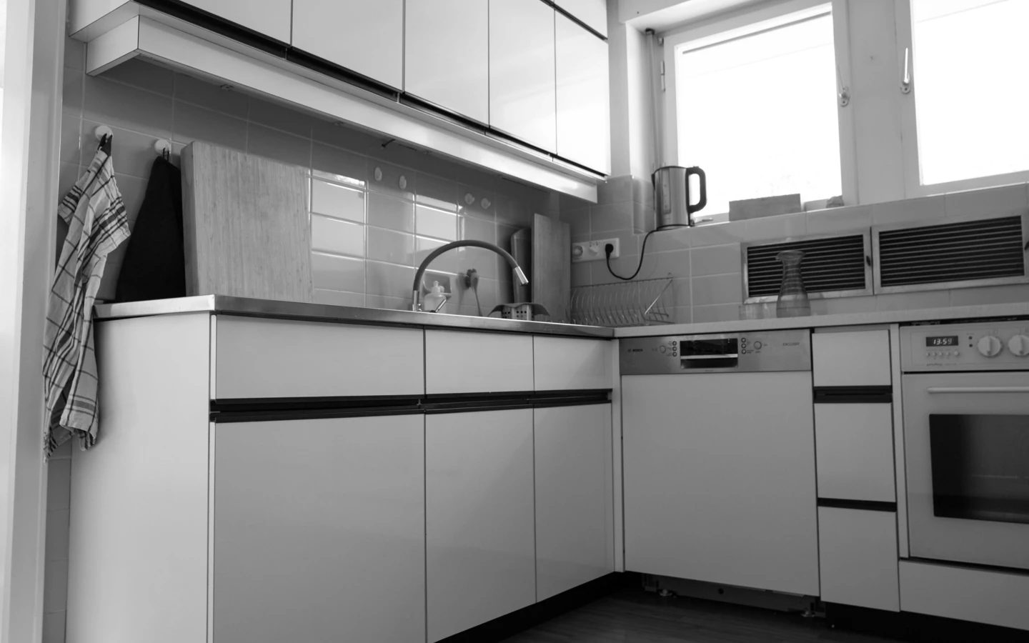 Eine schwarz-weiße Aufnahme einer modernen Küche mit weißen Schränken, Spüle, Geschirrspüler und Ofen in Dornbirn (Generalsanierung, Einfamilienhaus, Holzoptik).