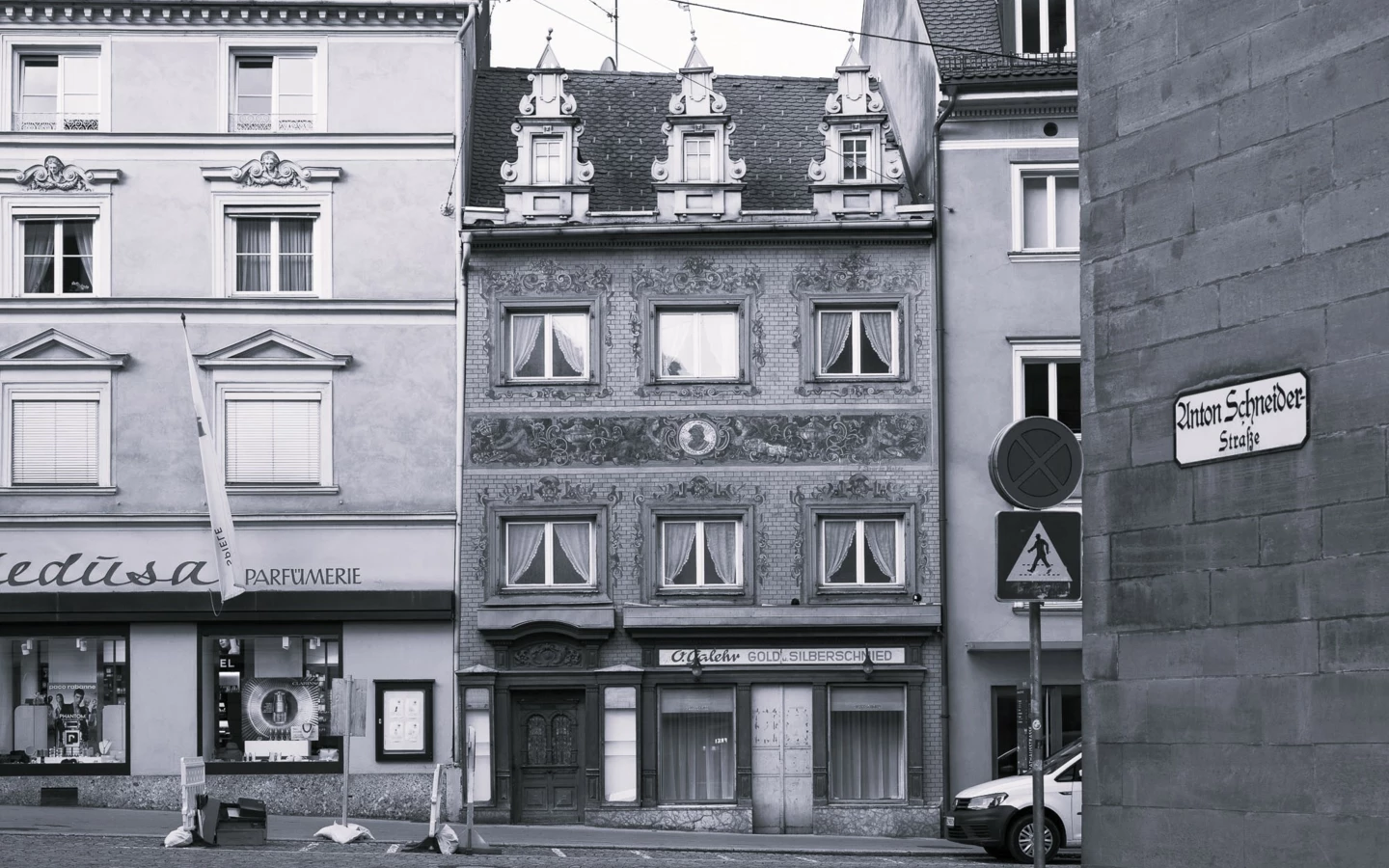 Die Anton-Schneider-Straße in Bregenz mit Gebäuden im Vordergrund, darunter ein altes, kunstvoll verziertes Haus und ein 'Medusa Parfumerie'-Laden (Rathausstr).