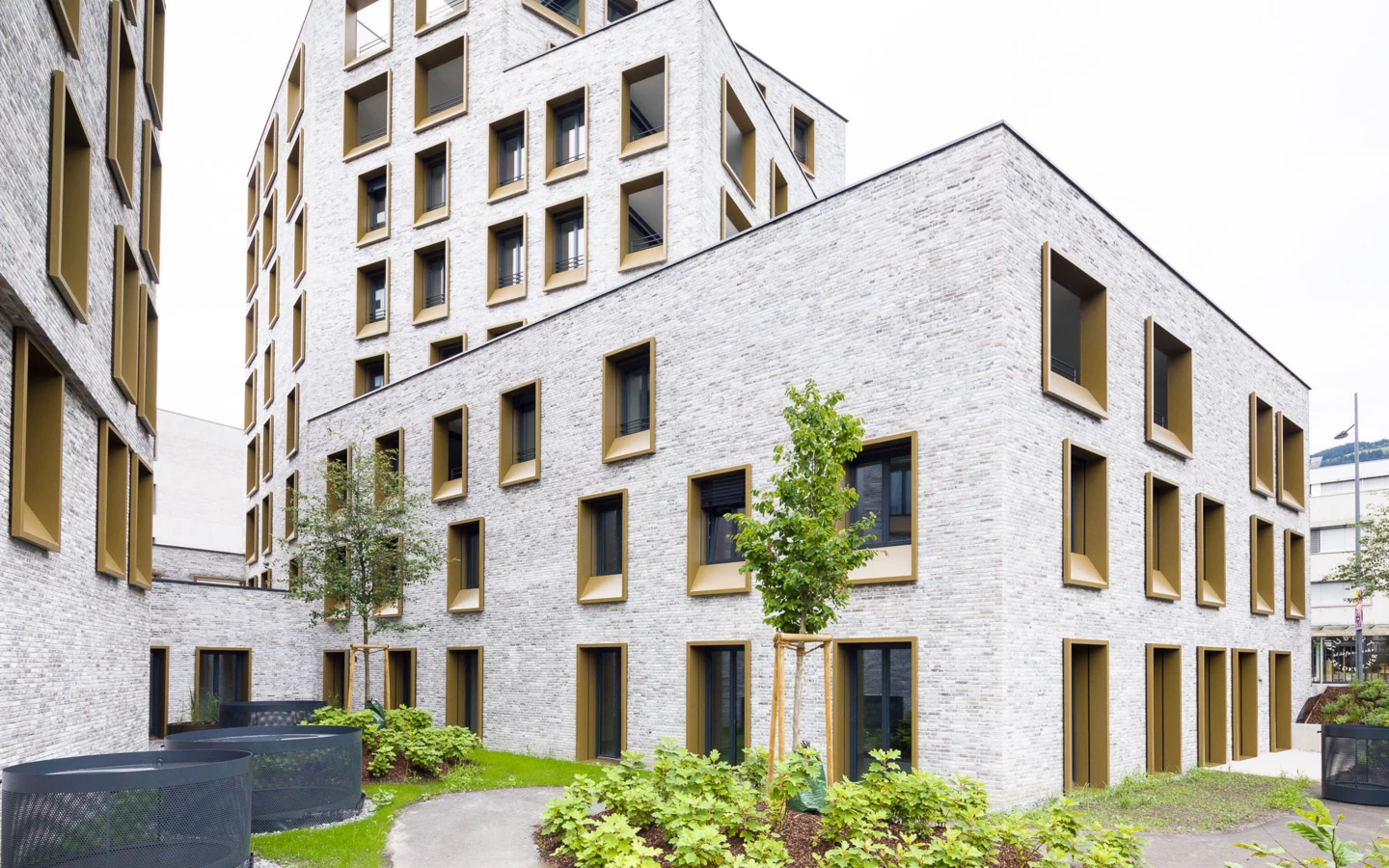 Moderne Gebäude des Wohnareals Kreuzgasse in Dornbirn mit hellen Ziegelfassaden und grün gerahmten Fenstern sowie begrünten Innenhöfen.