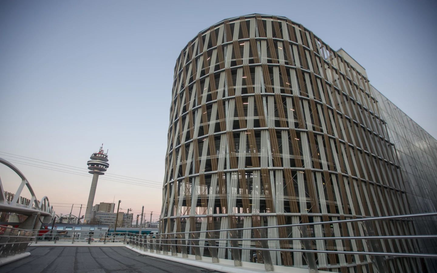 Gerundete Hochgarage am Wiener Hauptbahnhof mit einem Fernmeldeturm und Bahnsteigen im Hintergrund (Wien).