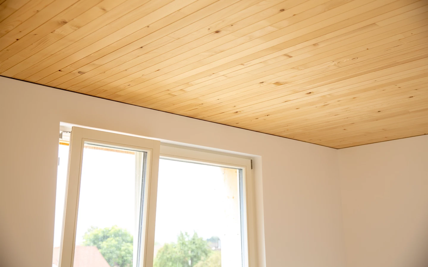 Natürliche Holzdecken in Innenräumen mit einem Fenster, das auf eine grüne Landschaft blickt, Neubau Hellbrunnerstraße (Hellbrunnenstraße).