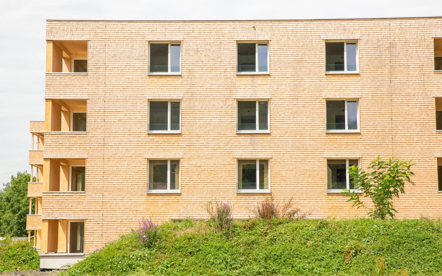 Mehrstöckiges Holzgebäude mit Holzschindelfassade, Fenstern und Balkonen, umgeben von grüner Vegetation an der Hellbrunner Straße (Hellbrunnenstraße).