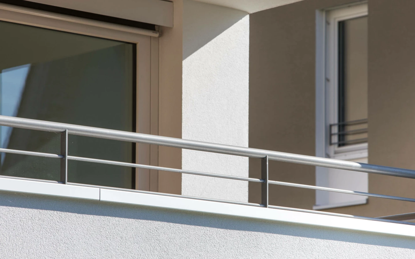 Balkon mit silbernem Geländer und Fenstern einer modernen Wohnanlage in Lustenau (Widum)