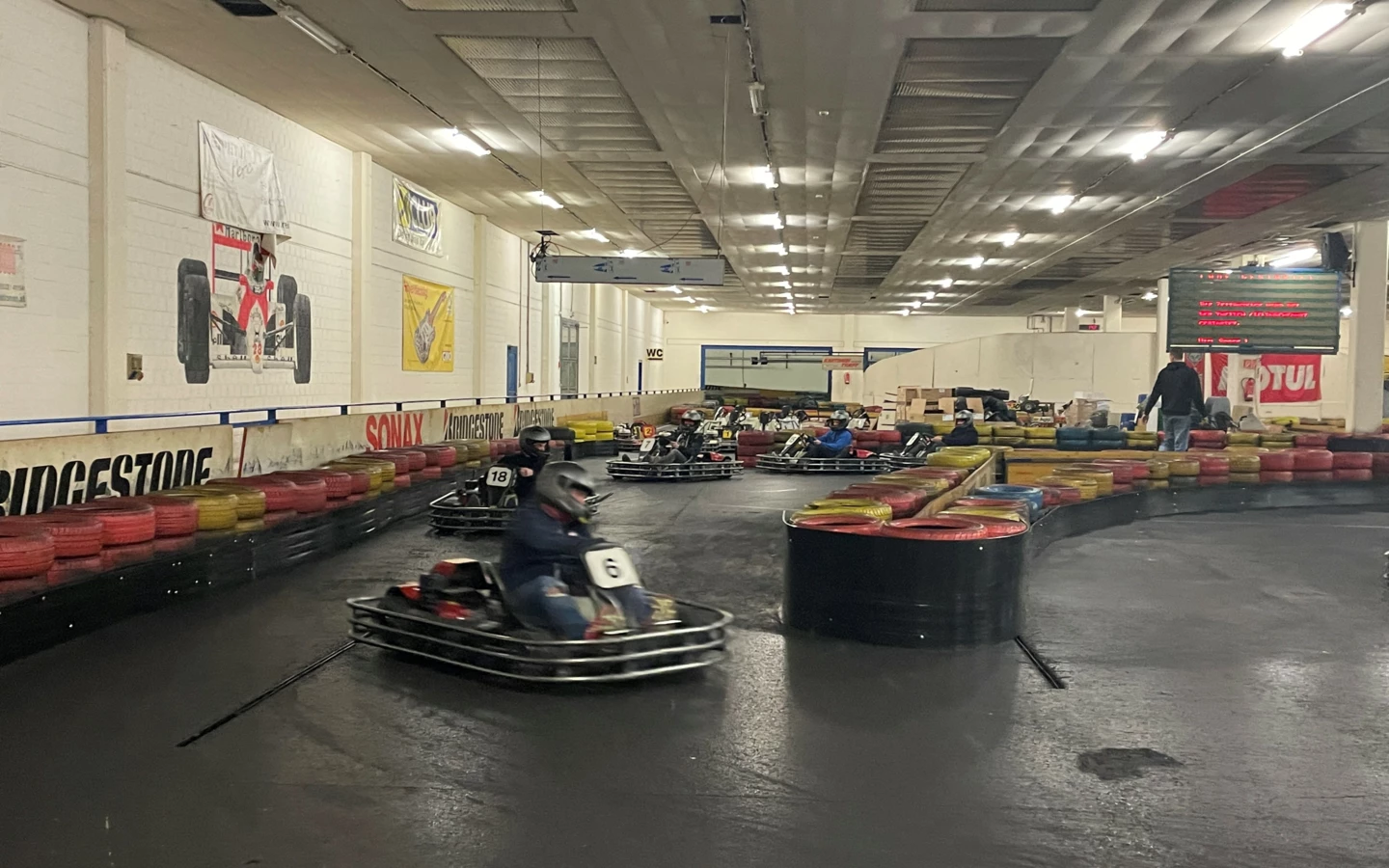 Mehrere Personen in Gokarts fahren auf einer Indoor-Rennstrecke mit Reifenbegrenzungen und Werbebannern an den Wänden (Lehrlingsabend).