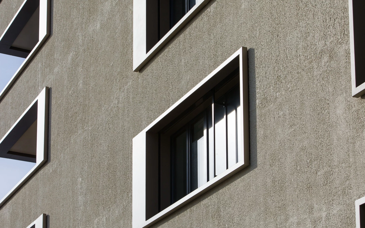 Fassade eines modernen Gebäudes mit strukturiertem Putz und schrägen Fenstern mit weißen Rahmen (Bäumleareal)