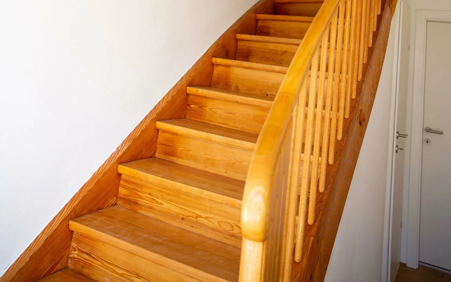 Eine elegante Holztreppe in einem Einfamilienhaus in Dornbirn, mit einer Topfpflanze auf einer Stufe und freiliegenden Glühbirnen an der Wand (Generalsanierung).