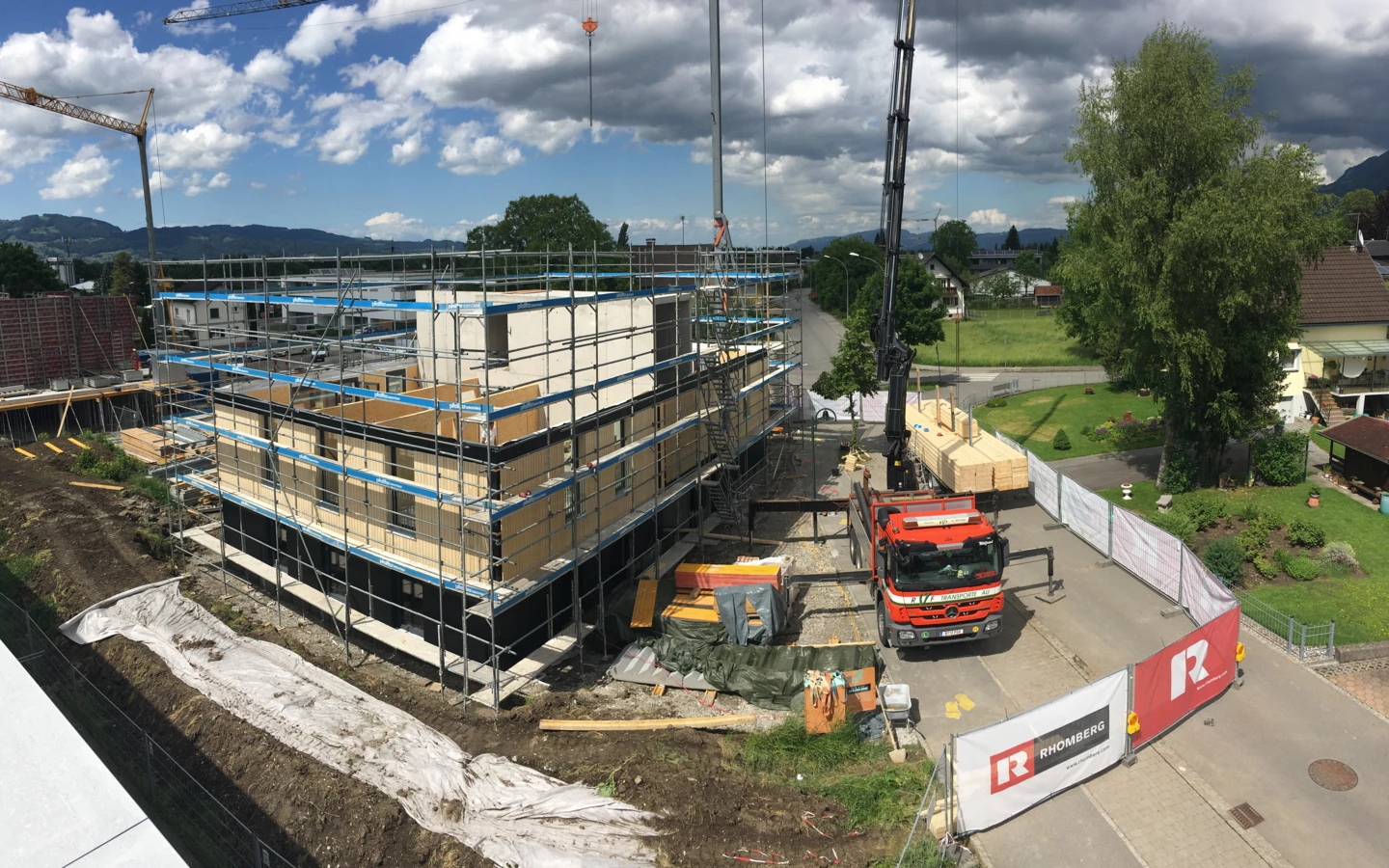 Holzbau-Projekt von Rhomberg Bau mit Gerüst, Baukran und Lieferwagen unter blauem Himmel mit Wolken (Architekturexkursionen, Holzbauprojekte).