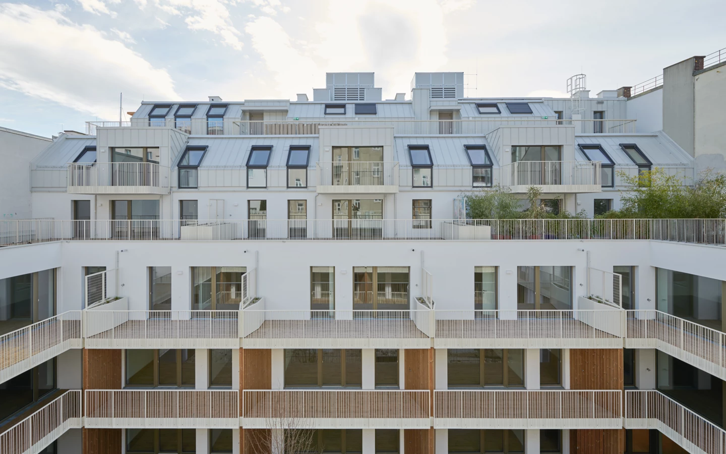 Ansicht des modernen Wohngebäudekomplexes Apollogasse 3 mit terrassierten Balkonen, Dachterrassen und Fenstern unter bewölktem Himmel.