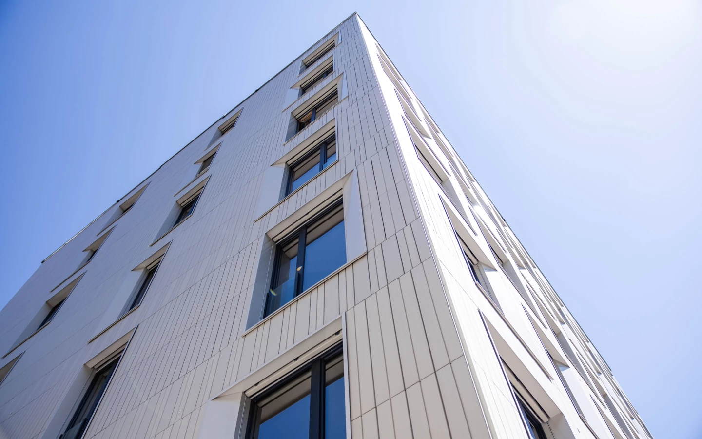 Modern building exterior with white paneled facade and numerous dark-framed windows reflecting the clear blue sky (Baerahus, Feldkirch)