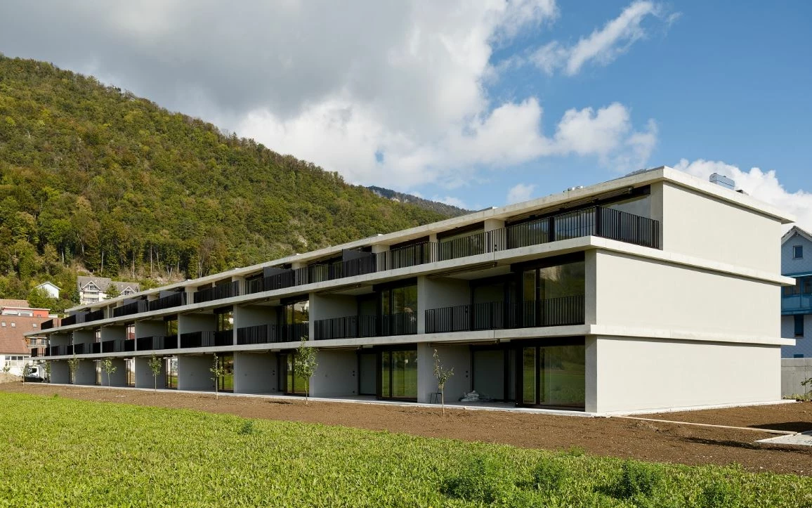 Moderne, mehrstöckige Wohnanlage in Egerkingen mit Balkonen, umgeben von einem grünen Feld und bewaldeten Hügeln unter blauem Himmel.