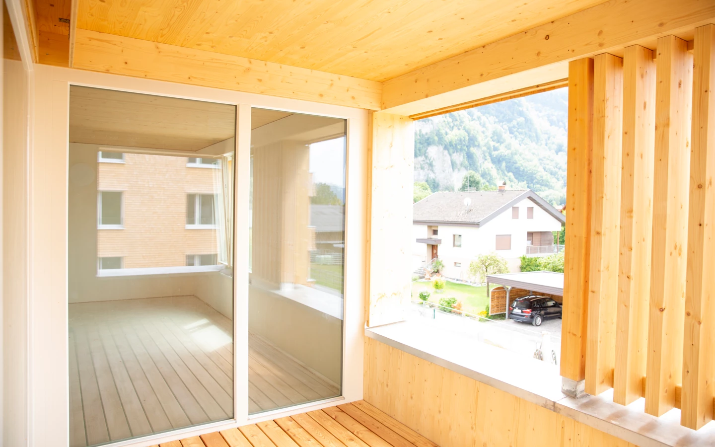Blick von einem Balkon aus Holz mit Glasschiebetüren auf ein Wohngebiet mit Häusern und einer bergigen Landschaft im Hintergrund (Hellbrunnenstraße).