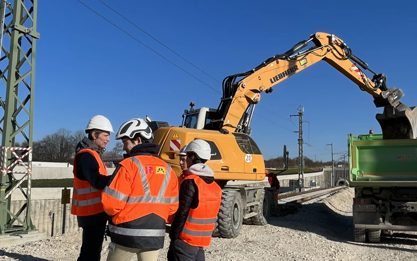 Bauarbeiter in Warnwesten vor Liebherr-Bagger beim Beladen eines Lkw (Rankweil, Deutschland)