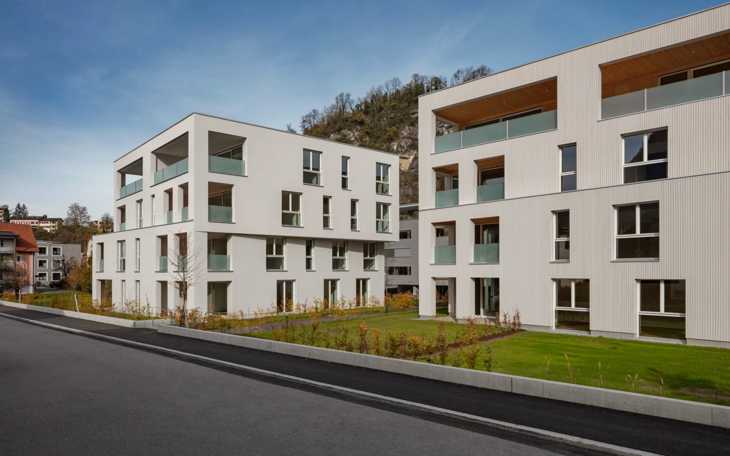 Zwei moderne weiße Wohngebäude mit Balkonen, umgeben von grünen Rasenflächen an der Zürcherstrasse in Bludenz (Wohnanlage).