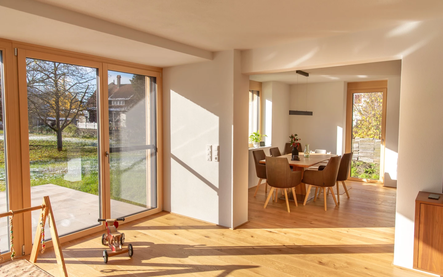Helles Wohn- und Esszimmer eines sanierten Einfamilienhauses mit Holzboden und Blick ins Grüne in Dornbirn (Generalsanierung, Holzoptik).