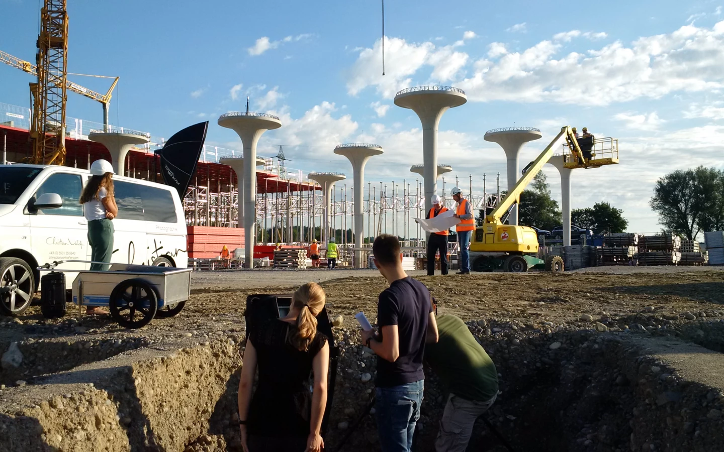 Arbeiter auf einer Baustelle mit vielen Betonsäulen und Kränen, während ein Fotoshooting stattfindet.