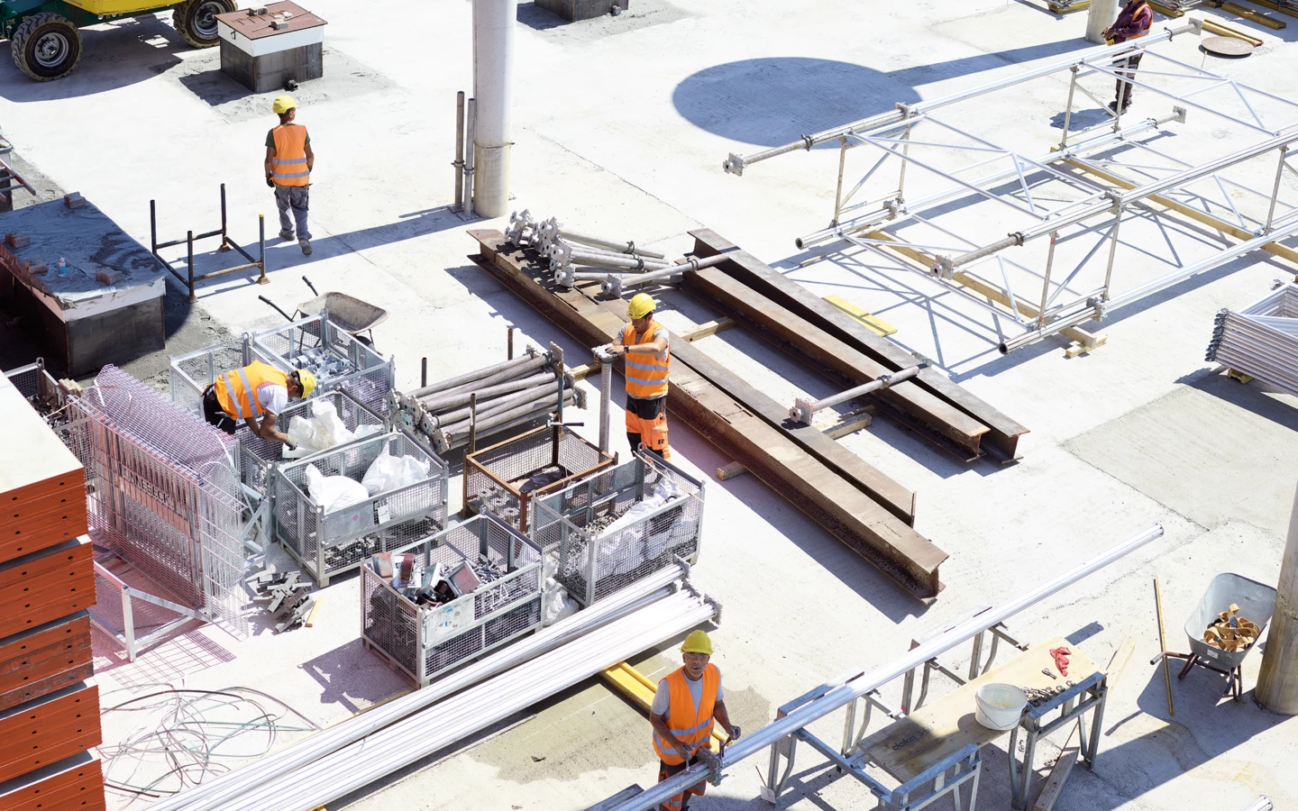 Arbeiter in Warnwesten und Schutzhelmen montieren Gerüstteile auf einer Baustelle der Rhomberg Bau GmbH bei Tageslicht (Bauarbeiten).