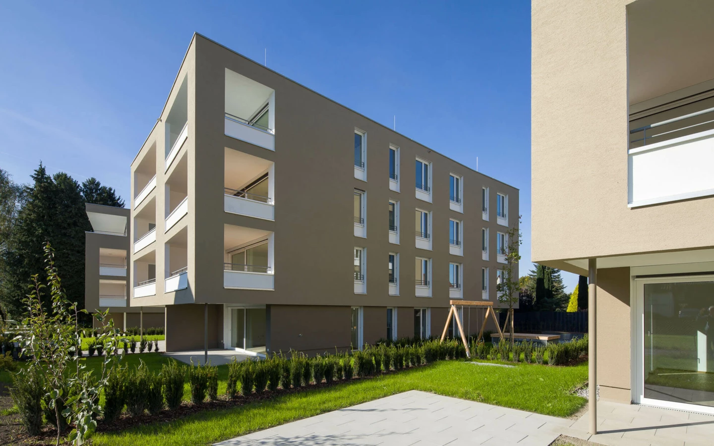 Moderne Wohnanlage Widum in Lustenau mit beigefarbener Fassade, Balkonen, Fenstern und gepflegter Grünfläche