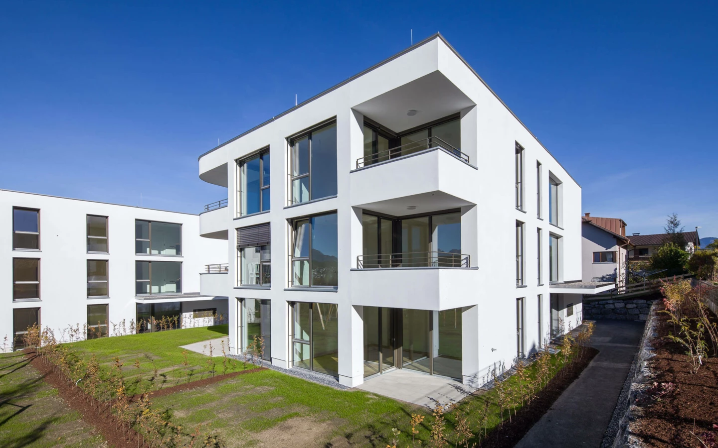 Moderne weiße Wohnanlage mit Balkonen und großen Fenstern unter blauem Himmel in Feldkirch (Wolf-Huber-Straße).