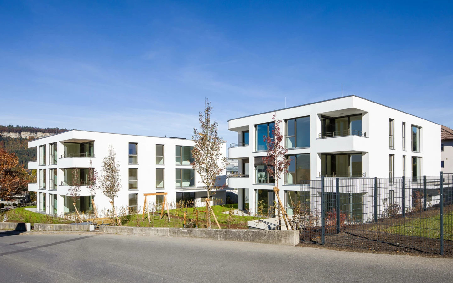 Zwei moderne weiße Wohngebäude mit großen Fenstern unter blauem Himmel in der Wohnanlage Wolf-Huber-Straße, Feldkirch.