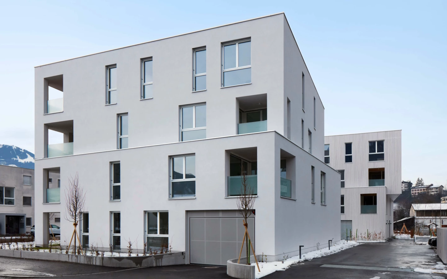 Aussenansicht der modernen Wohnanlage Zürcherstrasse Bludenz mit weißer Fassade, Balkonen und Garagentor an einem bewölkten Tag.