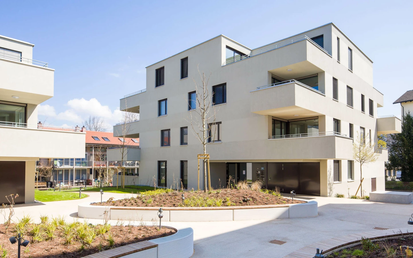 Moderne Wohnanlage Wuhrbaumweg von Rhomberg Bau mit hellen Fassaden, Balkonen und gepflegten Grünflächen unter blauem Himmel