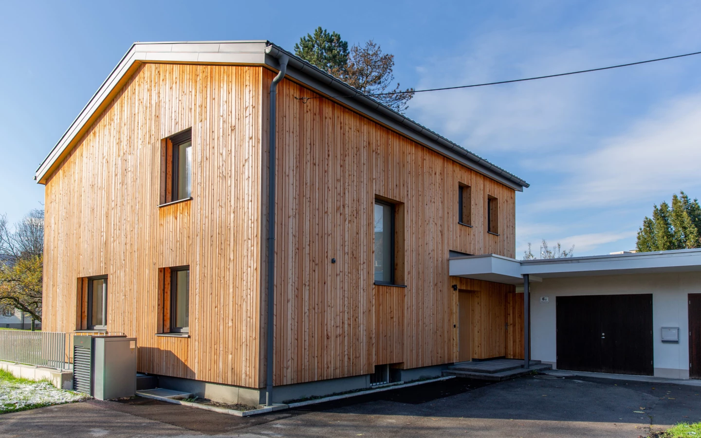 Modernes Einfamilienhaus in Dornbirn mit Holzfassade, mehreren Fenstern und angrenzender weißer Garage (Generalsanierung, Holzoptik).