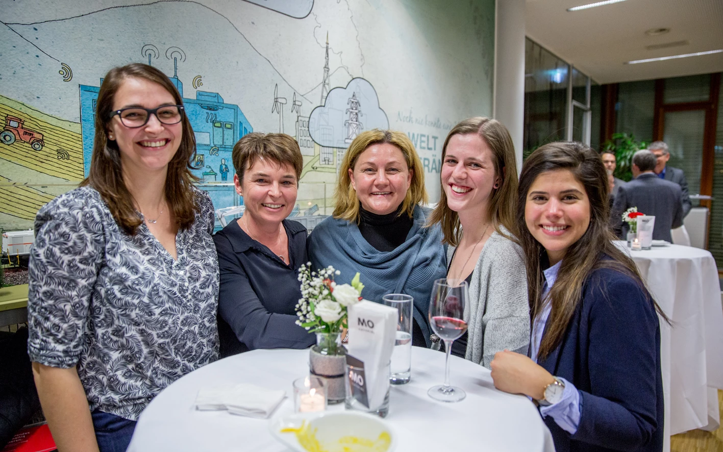 Fünf Frauen sitzen lachend an einem Stehtisch mit Getränken bei einer Veranstaltung, mit Wandgemälde im Hintergrund (Hubert, Geburtstag).