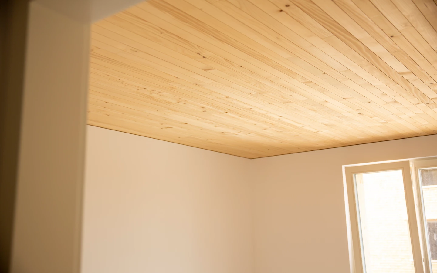 Eine helle Wand und eine Fensterfront in einem Zimmer mit einer Holzdecke an der Hellbrunnerstraße (Hellbrunnenstraße).