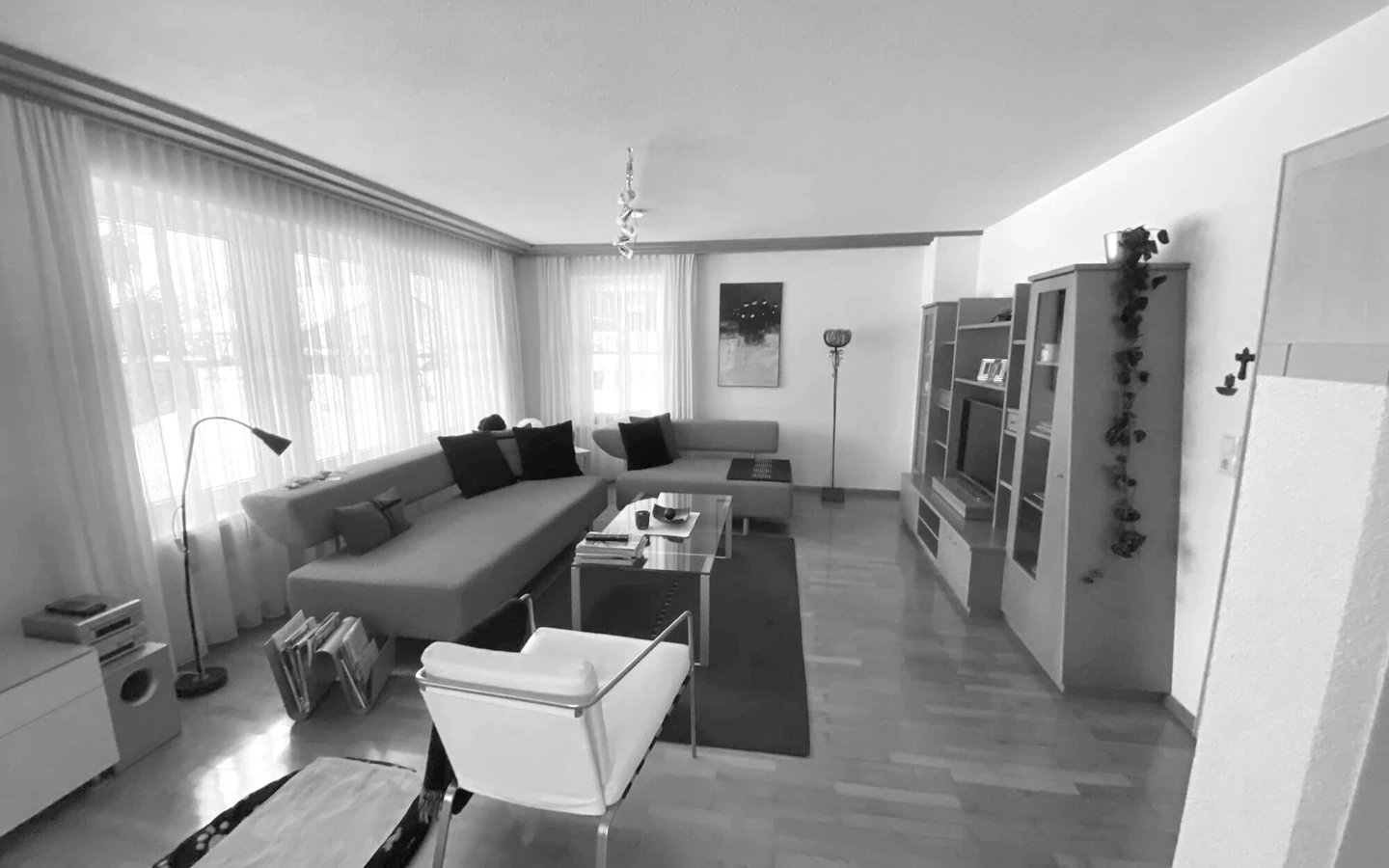 Wohnzimmer im Einfamilienhaus Bohle vor der Generalsanierung: Blick auf Polstermöbel, Couchtische, Teppich, weiße Stühle und Holzparkett.