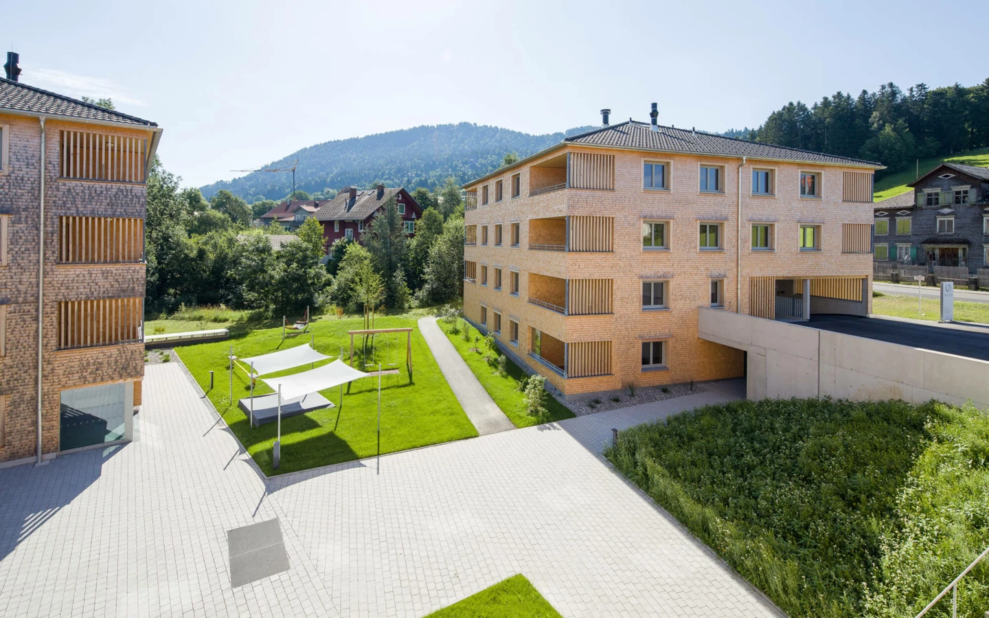 Moderne Wohnanlage Schwarz in Alberschwende mit Holzbalkonen und großzügiger Grünfläche am sonnigen Tag.