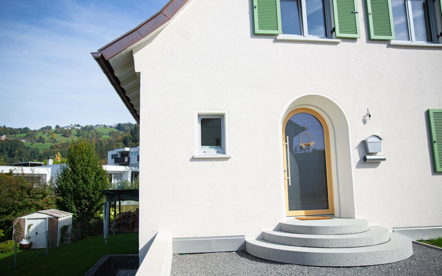 Eingangsbereich eines generalsanierten Einfamilienhauses in Dornbirn mit weißen Wänden, runden Betontreppen und modernem Holzeingang (Generalsanierung).