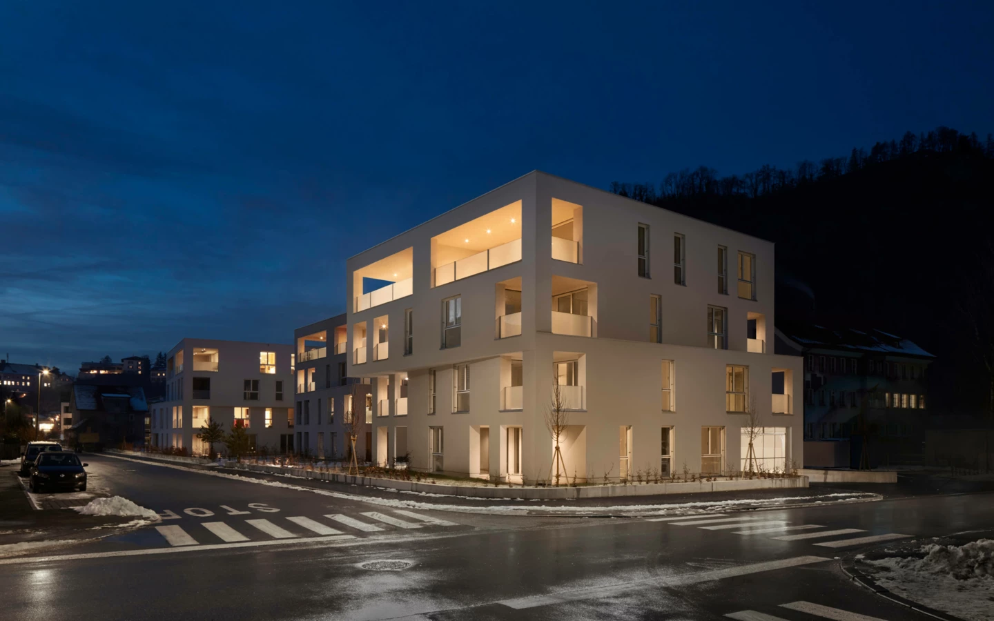 Moderne Wohnanlage Zürcherstrasse Bludenz bei Nacht mit beleuchteten Fassaden und Balkonen, Straßenkreuzung im Vordergrund.