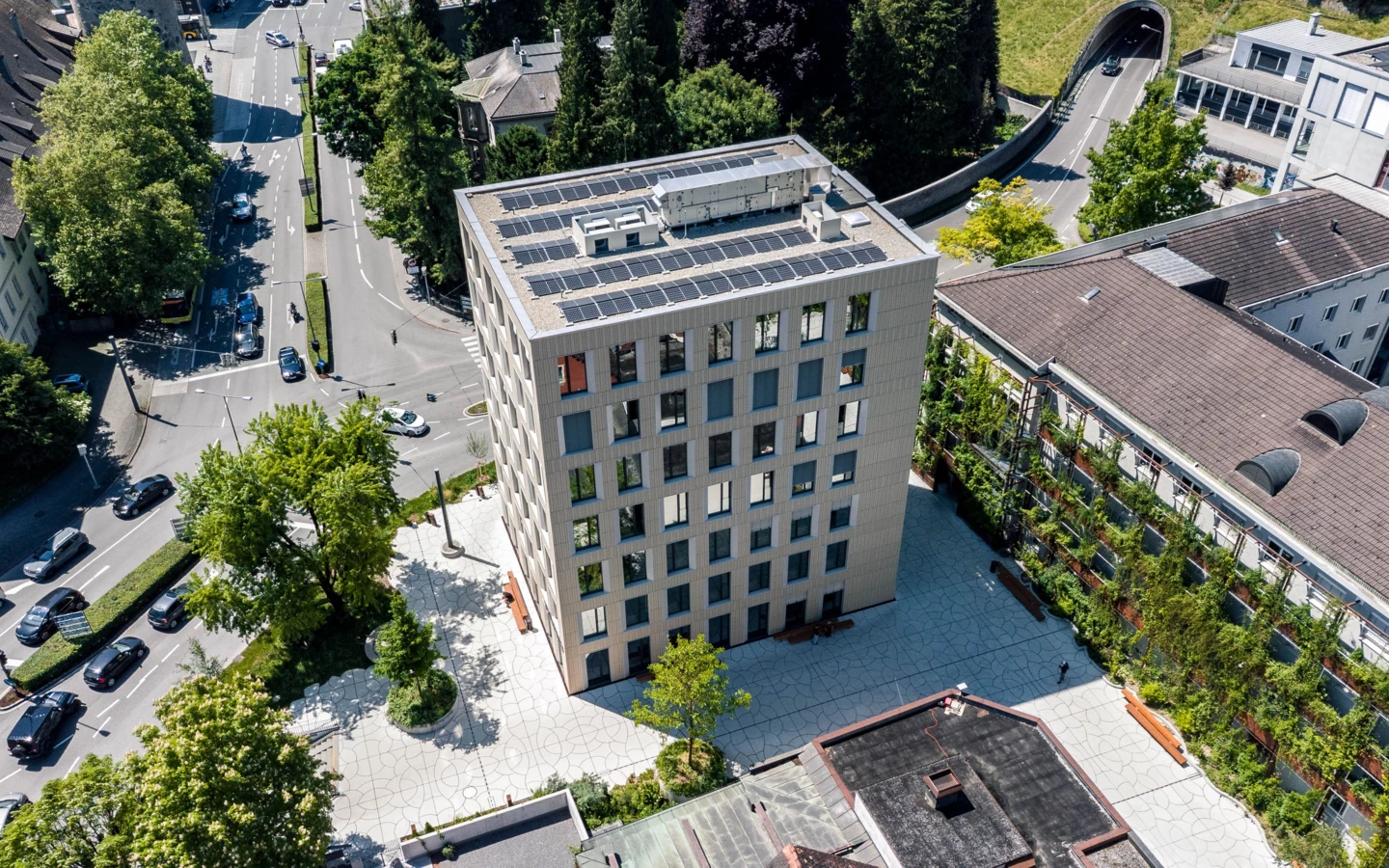 Aerial view of the Bärenhaus in Feldkirch, a modern multistory building with rooftop solar panels, amidst roads and trees (Baerahus).