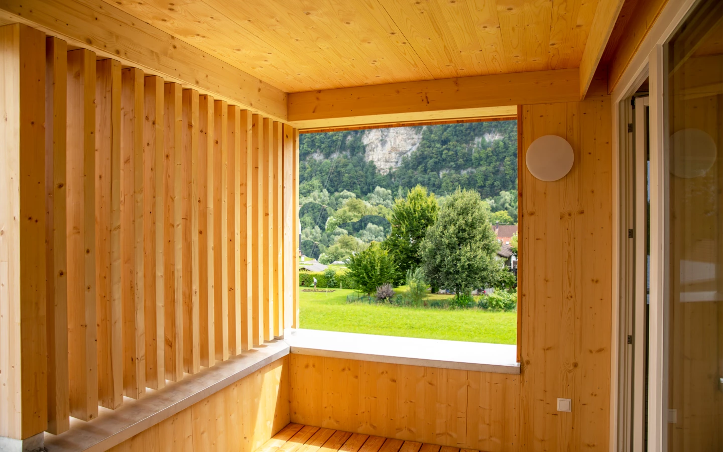 Holzverkleideter Balkon oder Loggia mit Blick auf grüne Wiesen, Bäume und einen bewaldeten Berg im Hintergrund (Hellbrunnenstraße).